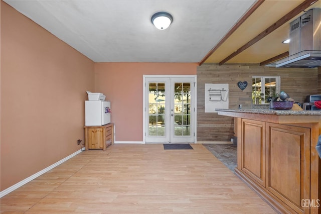 bar featuring beam ceiling, french doors, light wood-style flooring, wood walls, and baseboards