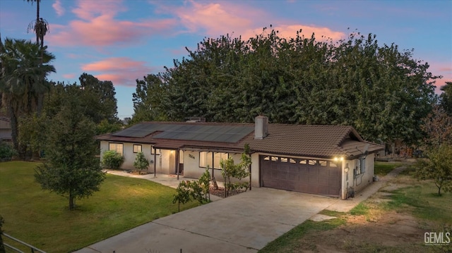 view of front facade featuring a garage, a tiled roof, driveway, a lawn, and roof mounted solar panels