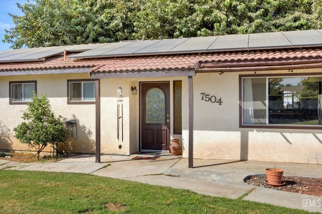 doorway to property featuring roof mounted solar panels, a tile roof, and stucco siding