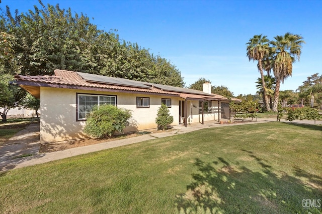 view of front of home featuring solar panels, a tile roof, a chimney, a front yard, and stucco siding