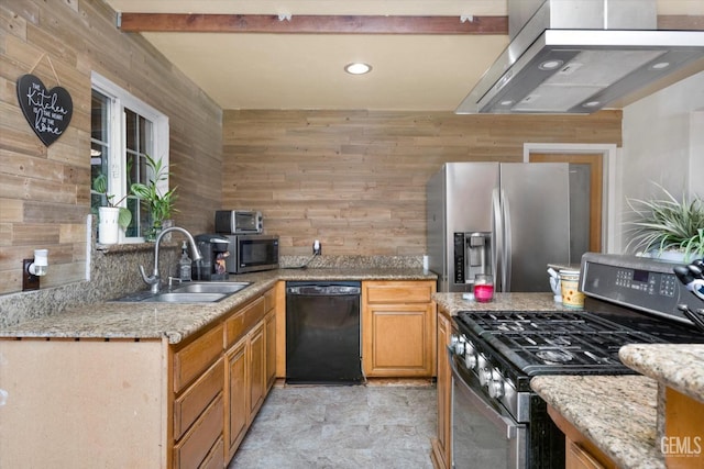 kitchen with light stone counters, appliances with stainless steel finishes, ventilation hood, wood walls, and a sink