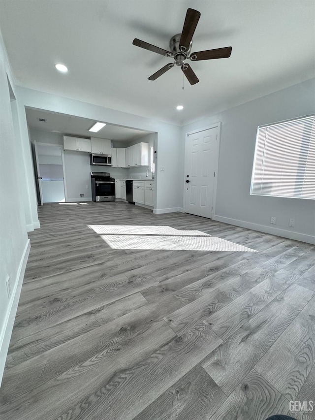 unfurnished living room with sink, ceiling fan, and light wood-type flooring