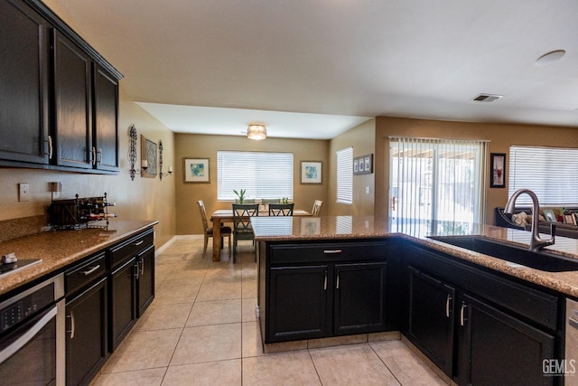 kitchen with stovetop, light tile patterned floors, oven, and sink