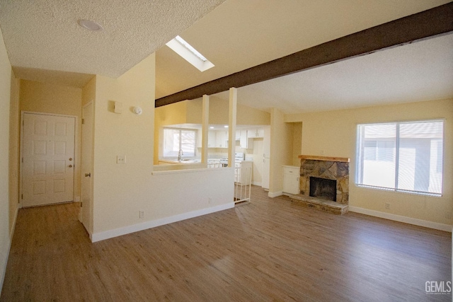 unfurnished living room featuring lofted ceiling with skylight, sink, a stone fireplace, and hardwood / wood-style flooring