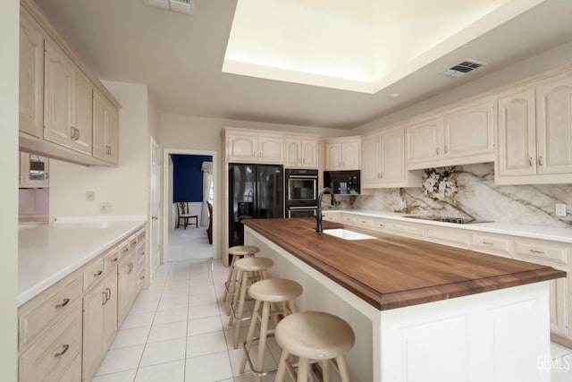 kitchen featuring sink, a breakfast bar area, wooden counters, black appliances, and an island with sink