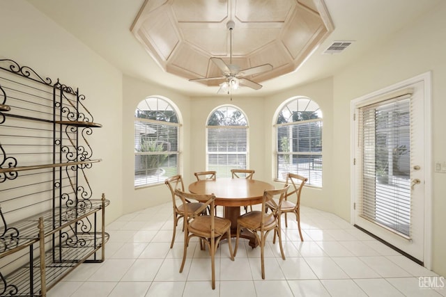 tiled dining area featuring ceiling fan, a raised ceiling, and a healthy amount of sunlight