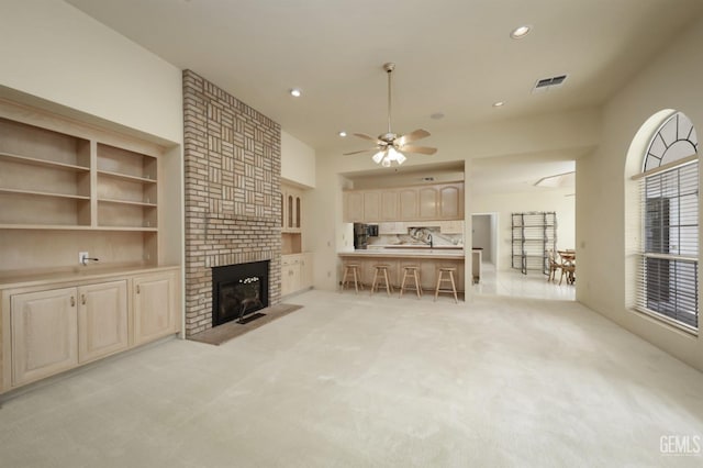 unfurnished living room featuring a brick fireplace, light carpet, and ceiling fan