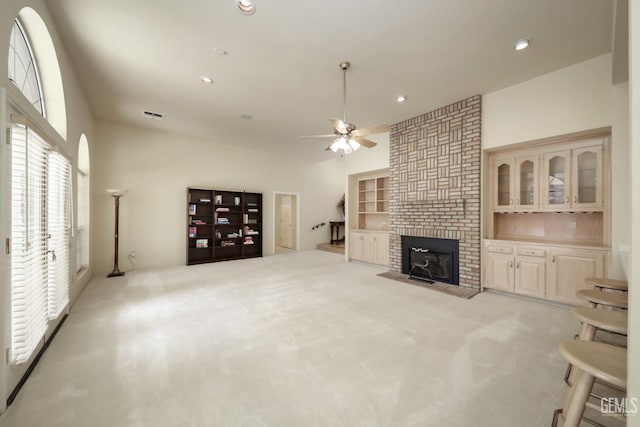 living room with a brick fireplace, built in features, light colored carpet, and ceiling fan