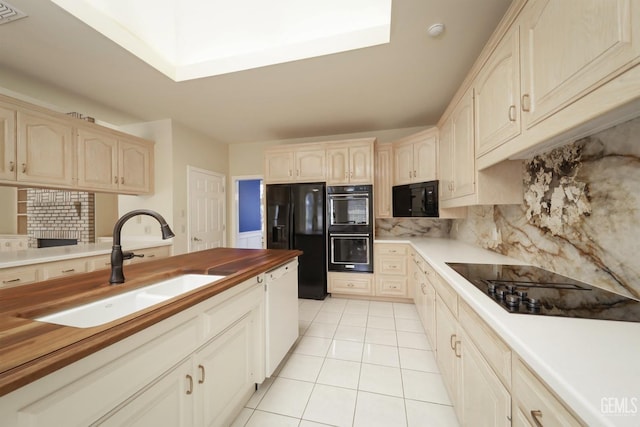 kitchen with butcher block countertops, sink, light tile patterned floors, decorative backsplash, and black appliances