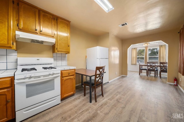 kitchen with tile counters, light wood-type flooring, white appliances, and backsplash