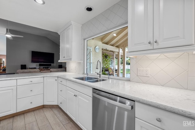 kitchen featuring light stone countertops, dishwasher, sink, vaulted ceiling, and white cabinets