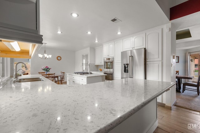 kitchen featuring sink, hanging light fixtures, stainless steel appliances, light stone counters, and a kitchen island