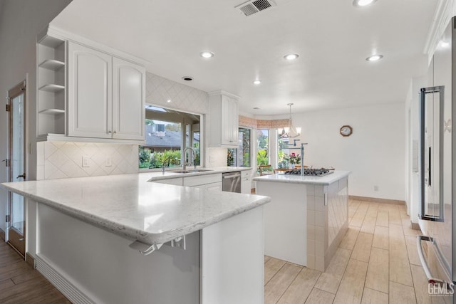 kitchen with white cabinetry, stainless steel appliances, kitchen peninsula, decorative light fixtures, and a kitchen island