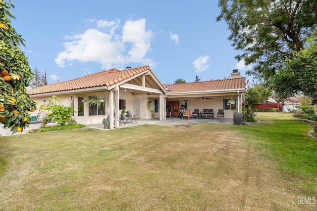 rear view of property featuring ceiling fan, a patio area, and a lawn