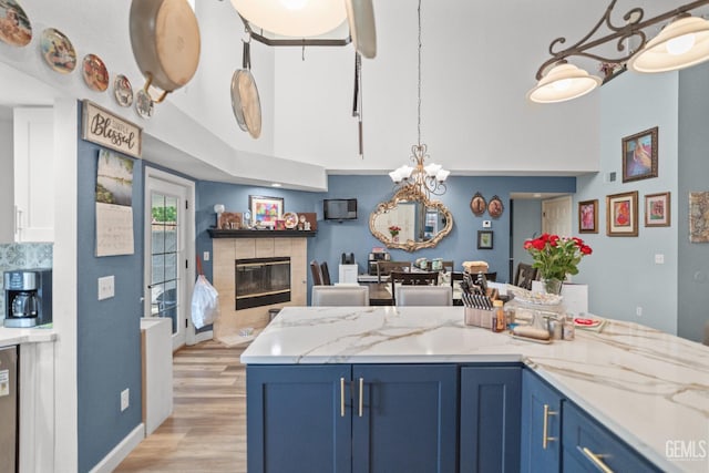 3809 Wensley Ct, Bakersfield, CA 93311 - kitchen with blue cabinets, a fireplace, light wood-style floors, a towering ceiling, and light stone counters