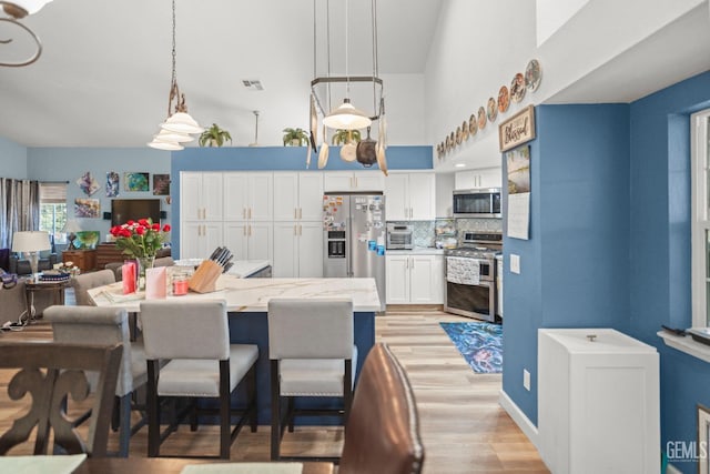 3809 Wensley Ct, Bakersfield, CA 93311 - kitchen featuring stainless steel appliances, light wood-style flooring, white cabinets, a breakfast bar area, and tasteful backsplash