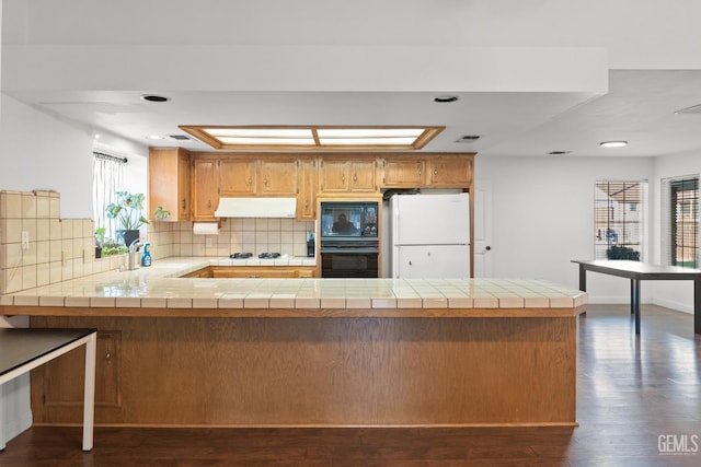 kitchen with white appliances, tile counters, kitchen peninsula, and plenty of natural light