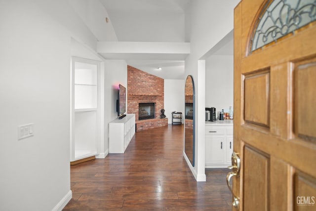 foyer with dark wood-type flooring, lofted ceiling with beams, and a brick fireplace