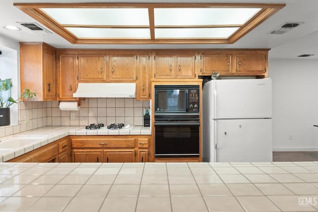 kitchen featuring backsplash, tile countertops, black appliances, and a skylight