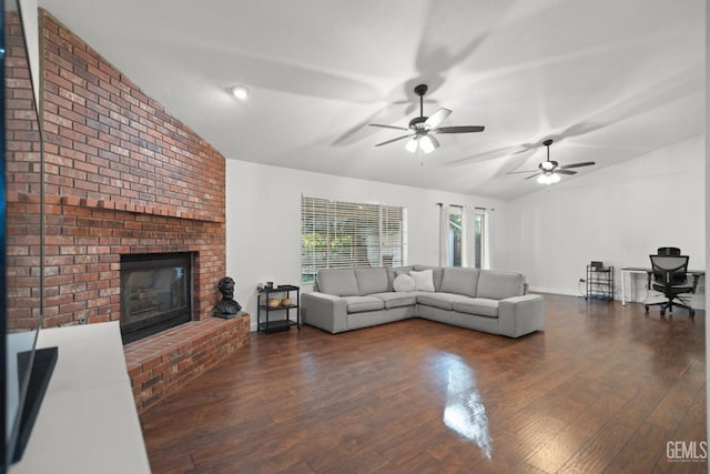 living room featuring vaulted ceiling, a brick fireplace, dark wood-type flooring, and ceiling fan