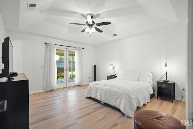 bedroom featuring light hardwood / wood-style flooring, ceiling fan, a tray ceiling, access to outside, and french doors