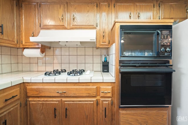 kitchen featuring tasteful backsplash, tile counters, ventilation hood, and black appliances