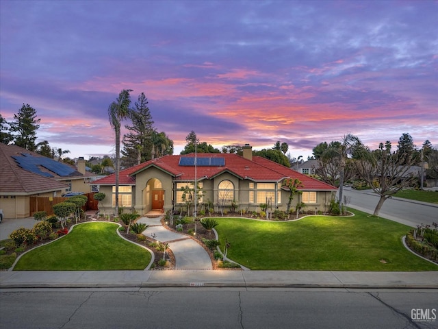 mediterranean / spanish home featuring stucco siding, a yard, a tiled roof, and solar panels