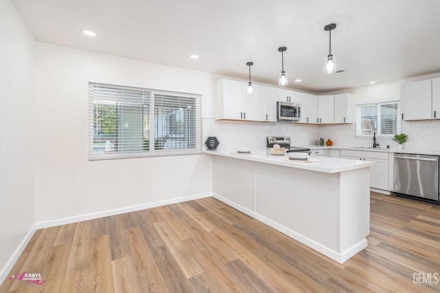 kitchen featuring pendant lighting, light hardwood / wood-style flooring, white cabinetry, kitchen peninsula, and stainless steel appliances