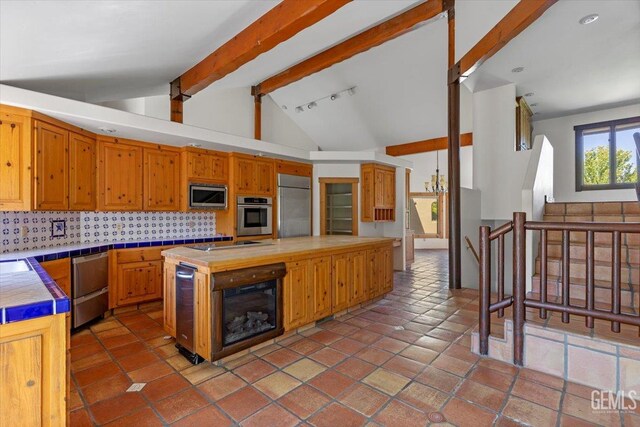 28221 Cumberland Rd, Tehachapi, CA 93561 - kitchen featuring appliances with stainless steel finishes, tile counters, decorative backsplash, a center island, and brown cabinetry