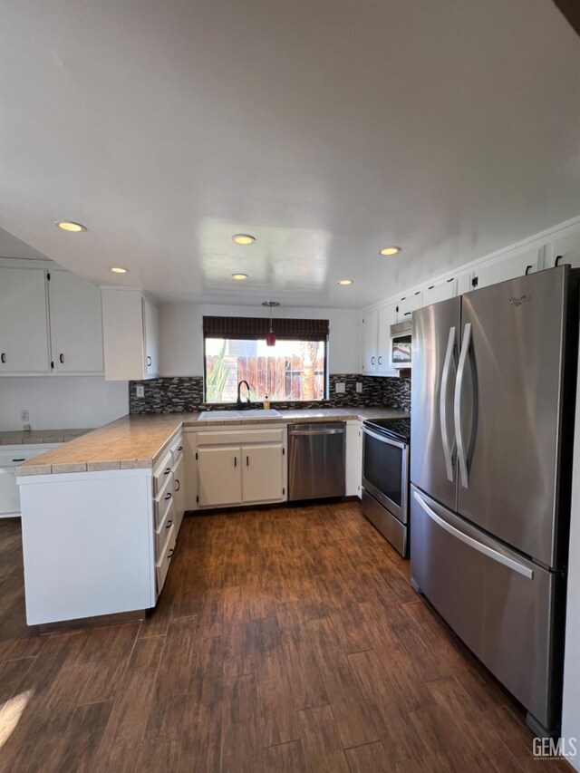 kitchen with stainless steel appliances, a sink, decorative backsplash, dark wood-style floors, and white cabinetry