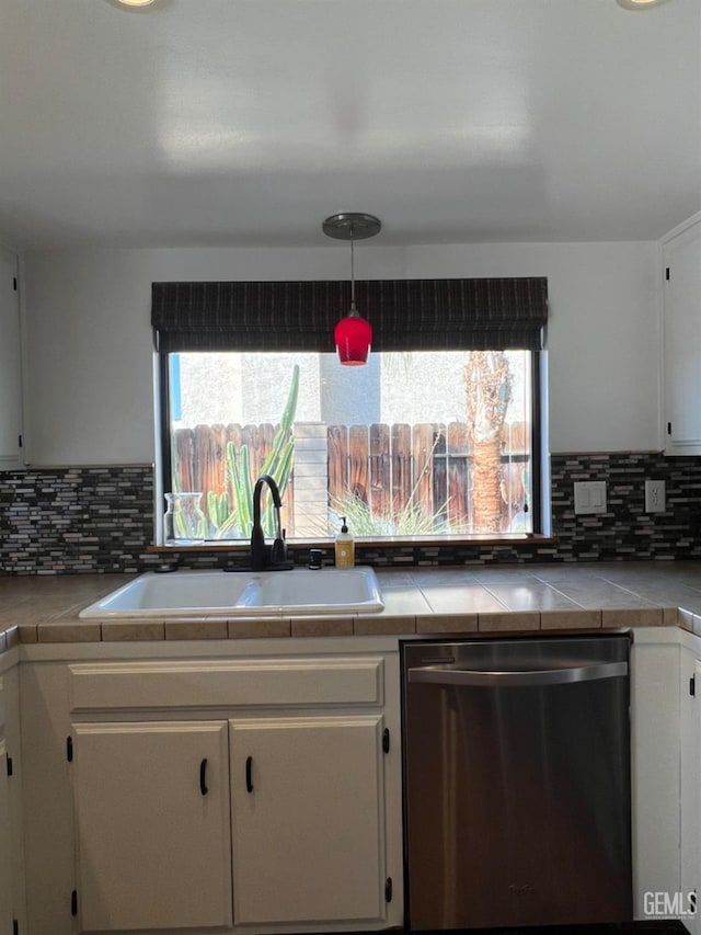 kitchen featuring stainless steel dishwasher, a sink, tile counters, and white cabinets