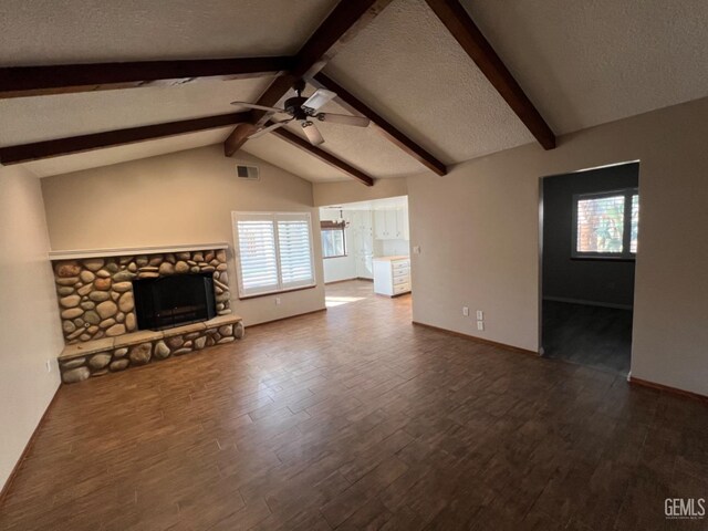 unfurnished living room featuring a ceiling fan, dark wood-type flooring, a textured ceiling, a stone fireplace, and baseboards