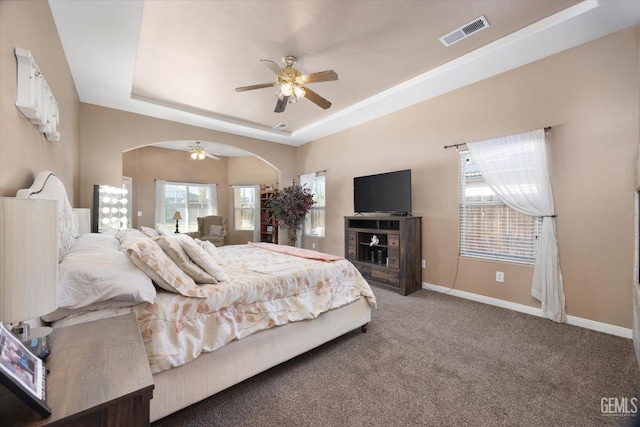 carpeted bedroom with ceiling fan and a raised ceiling