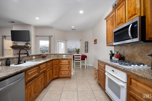 kitchen with light tile patterned flooring, sink, tasteful backsplash, stone counters, and stainless steel appliances