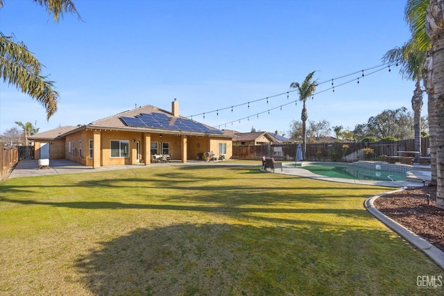 rear view of property with a lawn, a fenced in pool, a patio, and solar panels