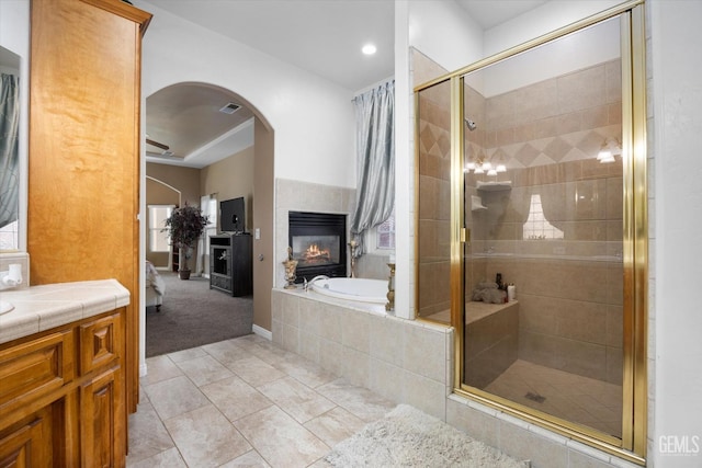 bathroom featuring a multi sided fireplace, vanity, plus walk in shower, and tile patterned floors