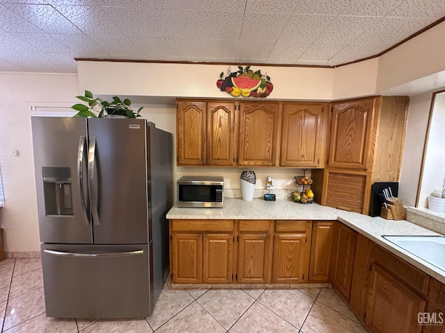1022 9th Ave, Delano, CA 93215 - kitchen with stainless steel appliances, brown cabinetry, light countertops, crown molding, and light tile patterned floors