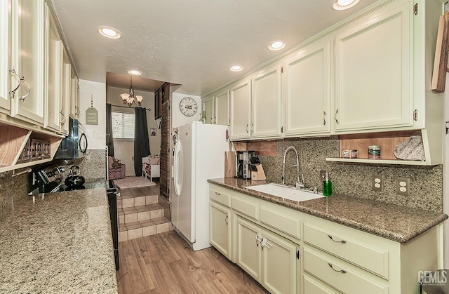 kitchen with black appliances, a sink, backsplash, an inviting chandelier, and light wood finished floors