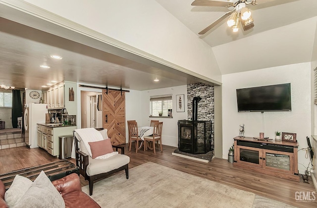 living room featuring a ceiling fan, wood finished floors, lofted ceiling, a wood stove, and a barn door