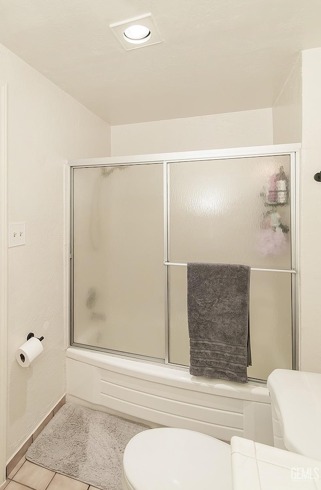 bathroom featuring tile patterned floors, toilet, baseboards, and shower / bath combination with glass door