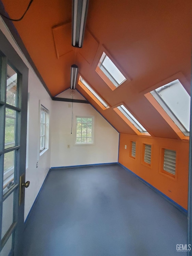 additional living space featuring lofted ceiling with skylight, concrete flooring, and baseboards