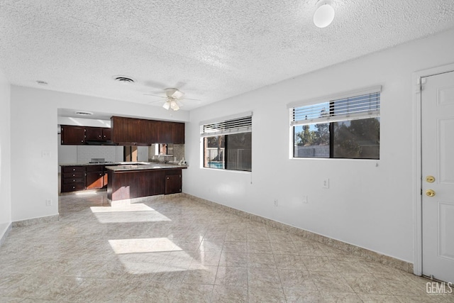 kitchen with ceiling fan, decorative backsplash, a textured ceiling, a kitchen island, and dark brown cabinetry