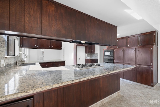 kitchen with oven, sink, light stone counters, black microwave, and stainless steel gas cooktop