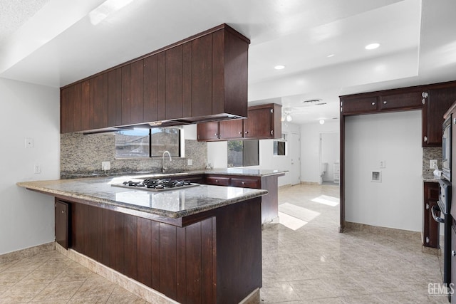 kitchen with stainless steel gas stovetop, kitchen peninsula, dark stone counters, and tasteful backsplash