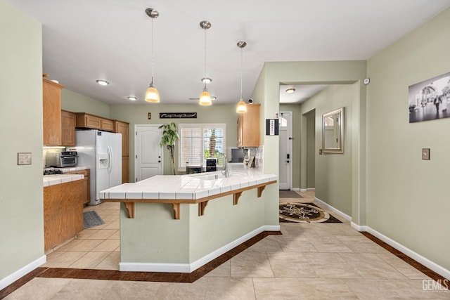 2109 Via Tuscania Ave, Delano, CA 93215 - kitchen featuring white fridge with ice dispenser, tile counters, a peninsula, baseboards, and light tile patterned floors