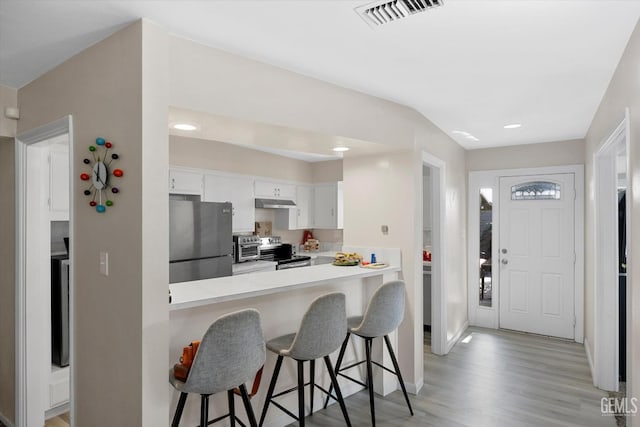 kitchen with white cabinetry, a kitchen bar, kitchen peninsula, stainless steel appliances, and light hardwood / wood-style flooring