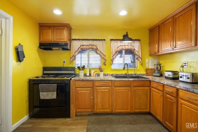 220 Tyler St, Taft, CA 93268 - kitchen with black gas range oven, under cabinet range hood, dark wood-type flooring, brown cabinetry, and recessed lighting