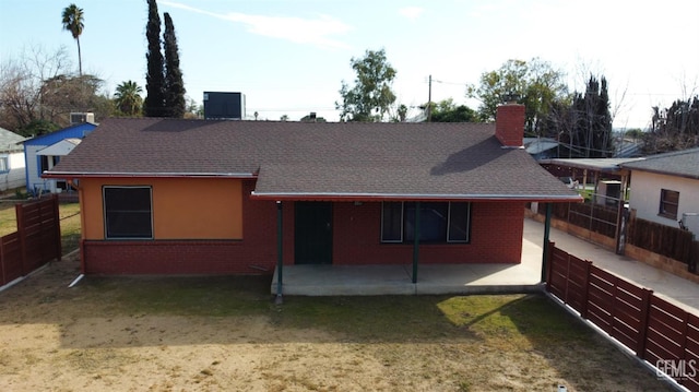 view of front of property featuring a patio area, brick siding, fence, and a chimney