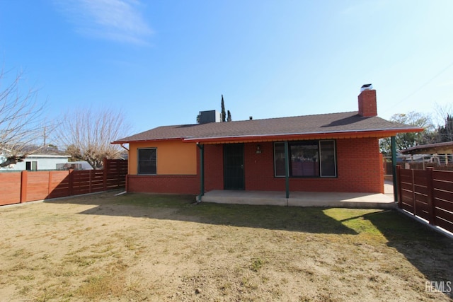 back of house with a patio, a fenced backyard, brick siding, a yard, and a chimney