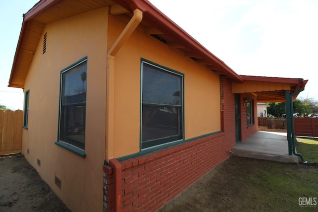 view of property exterior featuring brick siding, stucco siding, crawl space, a patio area, and fence